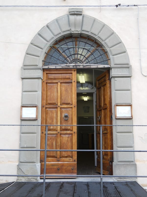 Arched wooden double doors set in a stone-framed entrance with a fanlight window above.