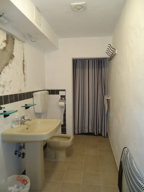A narrow bathroom with a pedestal sink, toilet, striped shower curtain, and tiled floor.