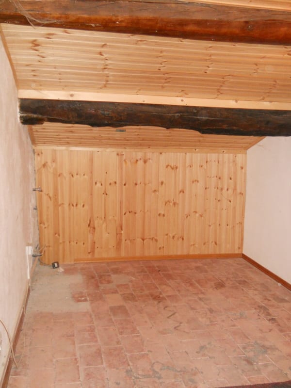 An empty attic-style room with fresh pine tongue-and-groove paneling on the wall and a rough-hewn ceiling beam.