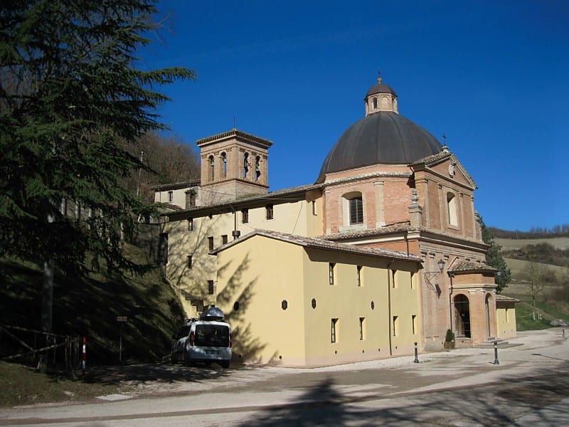 Exterior view of a yellow-walled Italian baroque church with a large dome, set against a clear blue sky.
