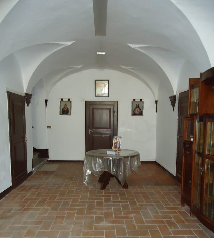 A vaulted entrance hall with terracotta tile floor, small side table with a cloth, and religious images on the walls.