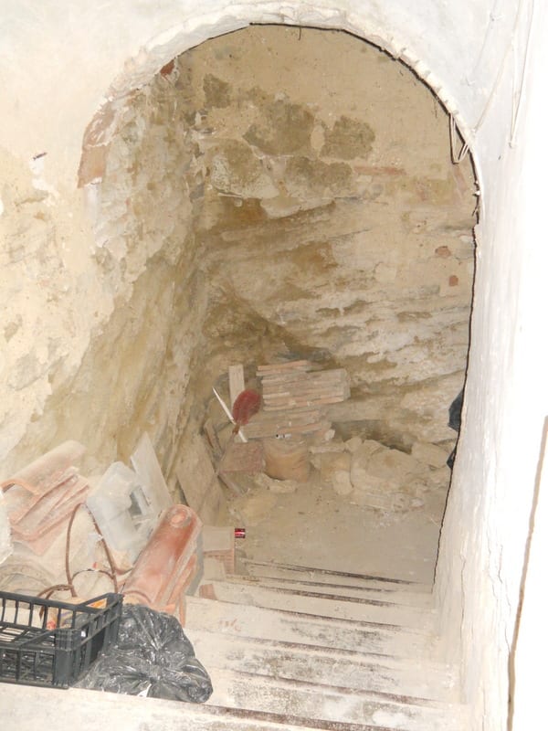 A worker's hand holding a trowel inside a rough arched opening with exposed brick and plaster, showing renovation in progress.