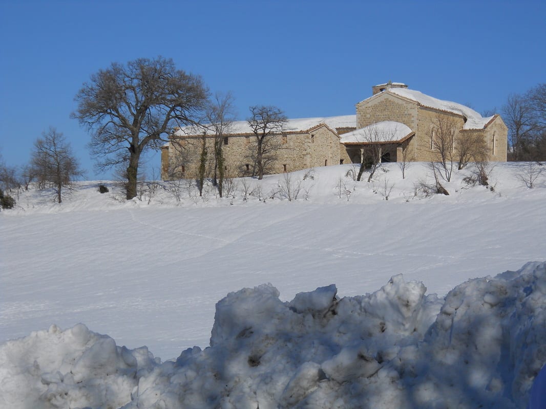 A stone building sitting atop a snowy hillside beneath a bright blue winter sky.
