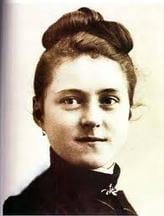 Colourised portrait photograph of Saint Thérèse of Lisieux as a young woman with her hair up, in a dark dress.