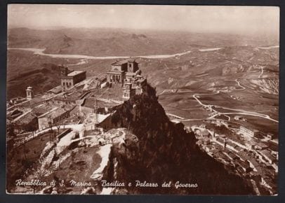 Sepia-toned vintage postcard of the Basilica and Palazzo del Governo of the Republic of San Marino perched on a rocky peak, with the inscription ‘Repubblica di S. Marino - Basilica e Palazzo del Governo.’