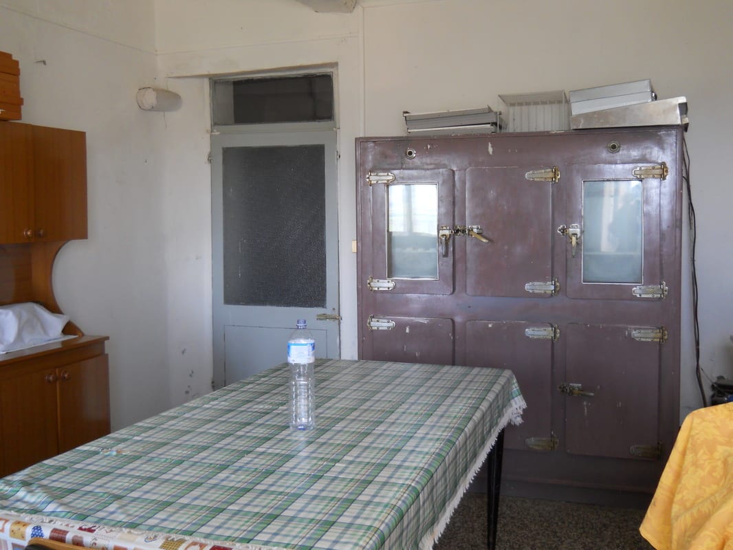 A bare room with an old wooden table, a large antique metal cabinet, and mismatched furniture awaiting clearing.