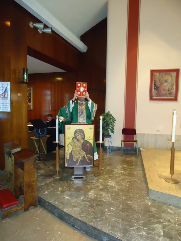 A bishop in purple vestments and mitre standing at the altar with an icon of the Mother of God on the ambo.