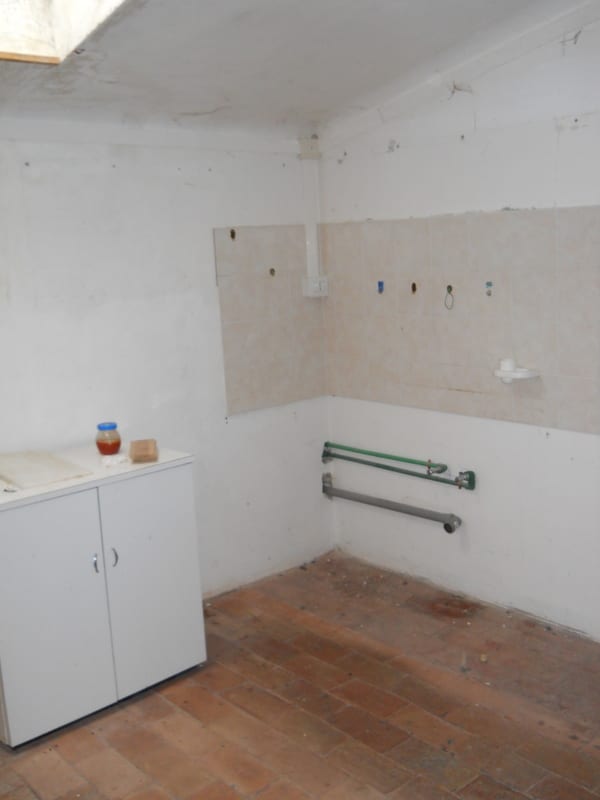 A bare, unfurnished room with damaged lower walls, a white cabinet, and grab bars already installed near the corner.