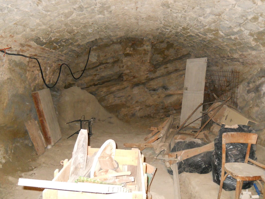 A vaulted stone cellar in rough condition, filled with debris, old wooden boards, and discarded furniture.