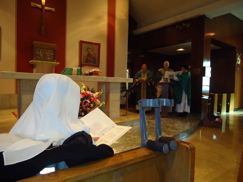 A sister prostrate on the floor of a modern church, arms extended, while a priest and ministers stand at the altar.