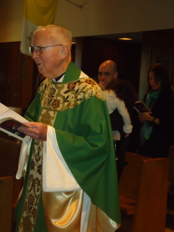 A priest in a green chasuble reads from a book at the ambo during a Mass celebrated in a small chapel.