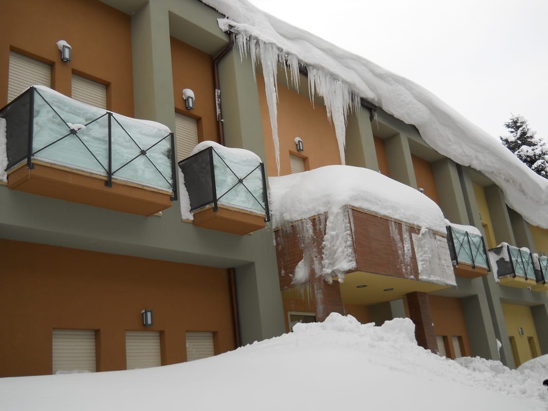 A two-story building exterior with balconies heavily laden with snow and large icicles hanging from the roofline.