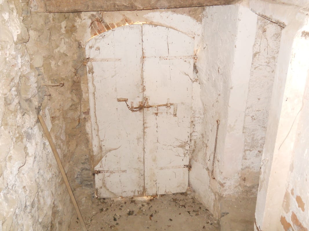 A derelict shower or utility enclosure with crumbling plaster walls and corroded pipework, before renovation.