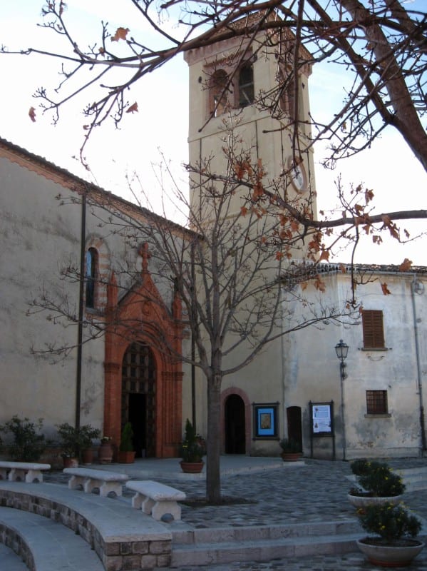 A stone church with a terracotta-trimmed portal and a square bell tower, surrounded by bare trees in winter.