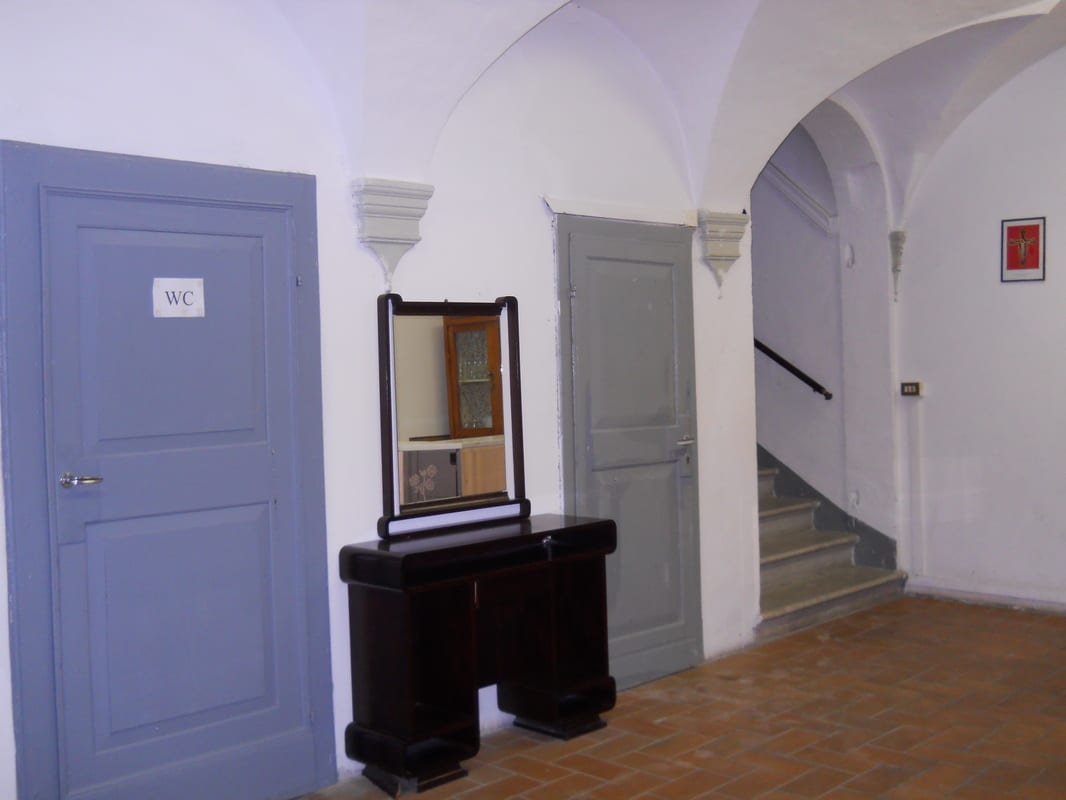 An arched entrance hall with grey-painted doors, a small antique dressing table with mirror, and a staircase visible through an archway.