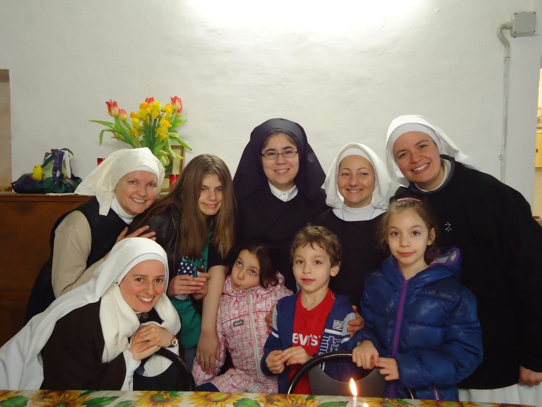 A group of sisters in black and white habits smiling with several children and young women around a candlelit table.