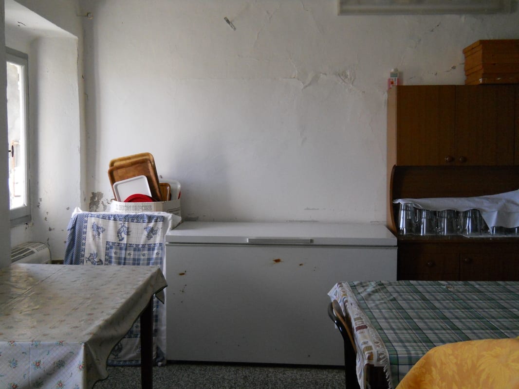 A sparse, run-down room with peeling walls, a chest freezer, old cabinets, and mismatched furniture awaiting clearance.