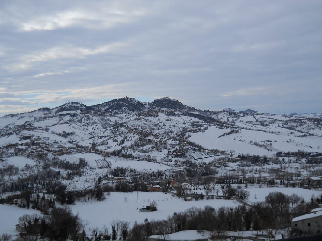 A wide panoramic view of snow-covered hills and valleys under a grey winter sky.