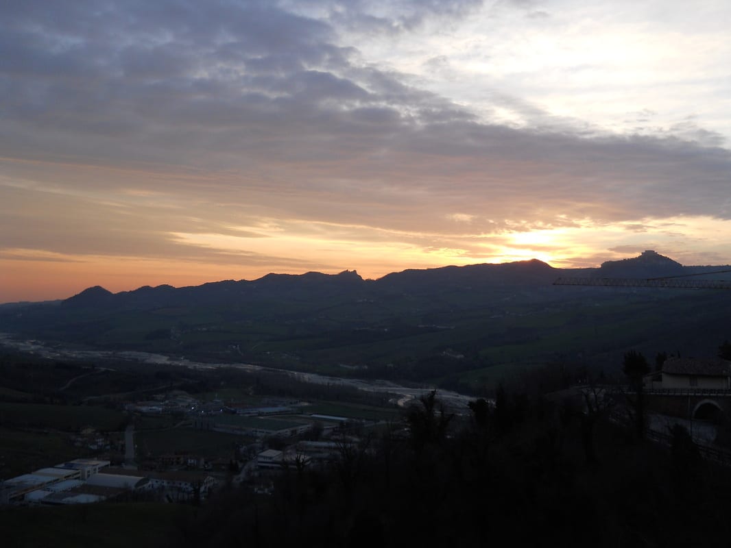 A wide sunset view over mountain silhouettes and a valley town, the sky streaked orange and purple.