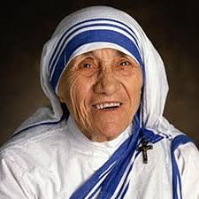 Close-up photograph of Saint Teresa of Calcutta smiling, wearing her white and blue-striped Missionaries of Charity sari with a small crucifix.