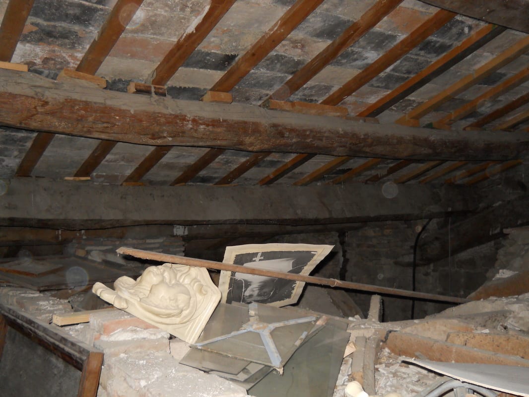 Exposed roof joists and rubble in a derelict attic space, with broken plaster and debris on the floor.
