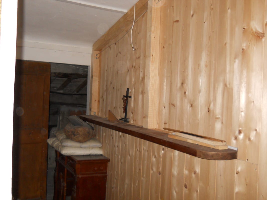 A narrow wooden-panelled alcove with a long shelf and a small crucifix mounted on the wall, with a chest of drawers visible in the adjacent space.