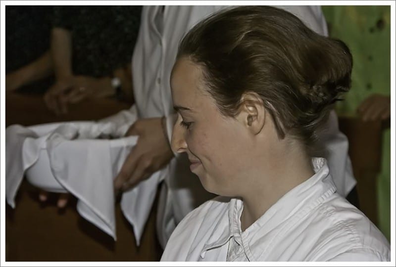 Close-up of a young woman with her hair up, head bowed, receiving her veil during an investment ceremony.