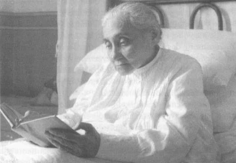Black-and-white photograph of the Servant of God Luisa Piccarreta lying propped in bed, reading a book.