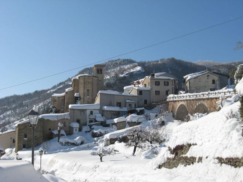 The snow-covered hilltop village of Talamello under a clear blue winter sky.