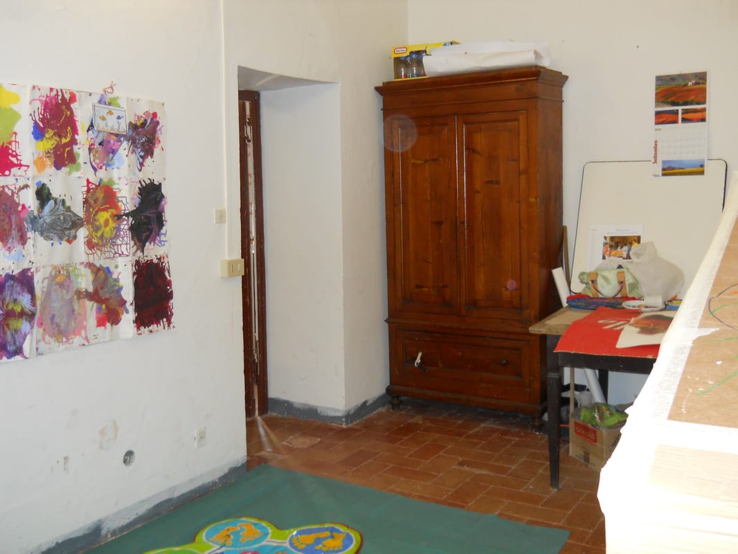 A cluttered room with tiled floor, a large wardrobe, a ladder, and various items stacked against the walls before renovation.