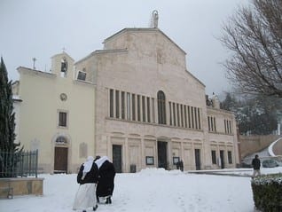 Two sisters in white habits walking toward a large snow-covered church facade.