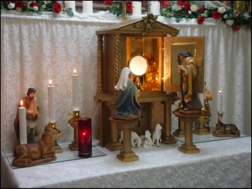 An indoor nativity display with painted figurines of the Holy Family, candles, and decorative garland on a draped table.