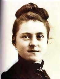 Sepia photograph of Saint Thérèse of Lisieux as a young woman, hair pinned up, in dark clothing, looking directly at the camera.