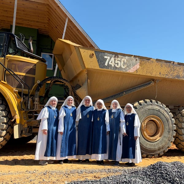 Six sisters stand together in front of a huge yellow dump truck on the building site.