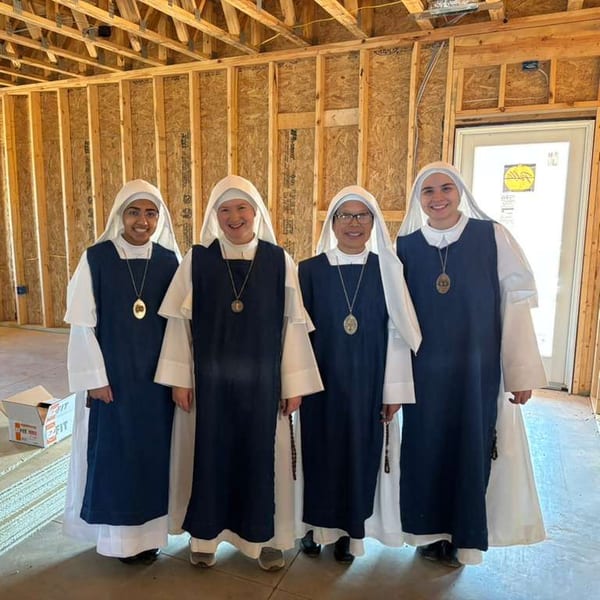 Four sisters smiling inside the timber frame of the new monastery.