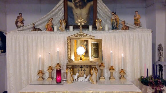A decorated altar set for adoration with a golden monstrance, candles, angels, and nativity figures, topped by a painting of the crucifixion.